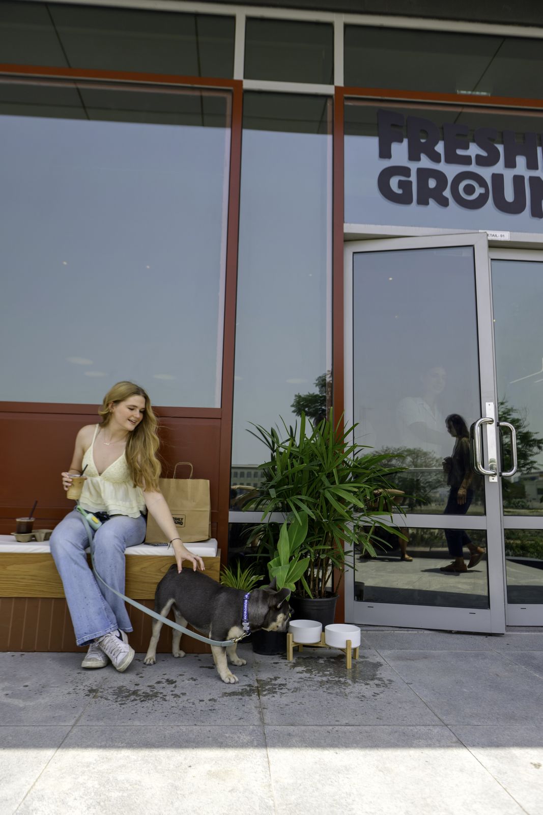 A guest with her French bulldog on a leash at the Freshly Ground entrance, next to the dedicated pet water bowls