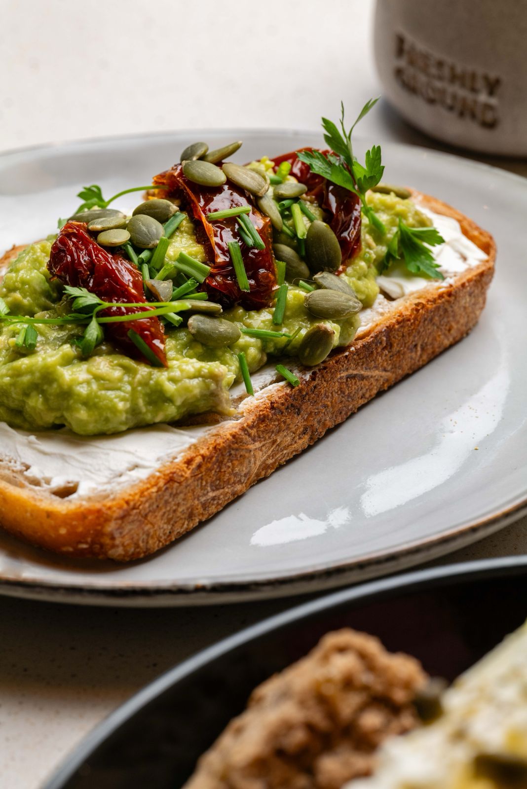 Smashed avocado toast on sourdough with sun-dried tomatoes, pumpkin seeds and herbs at Freshly Ground