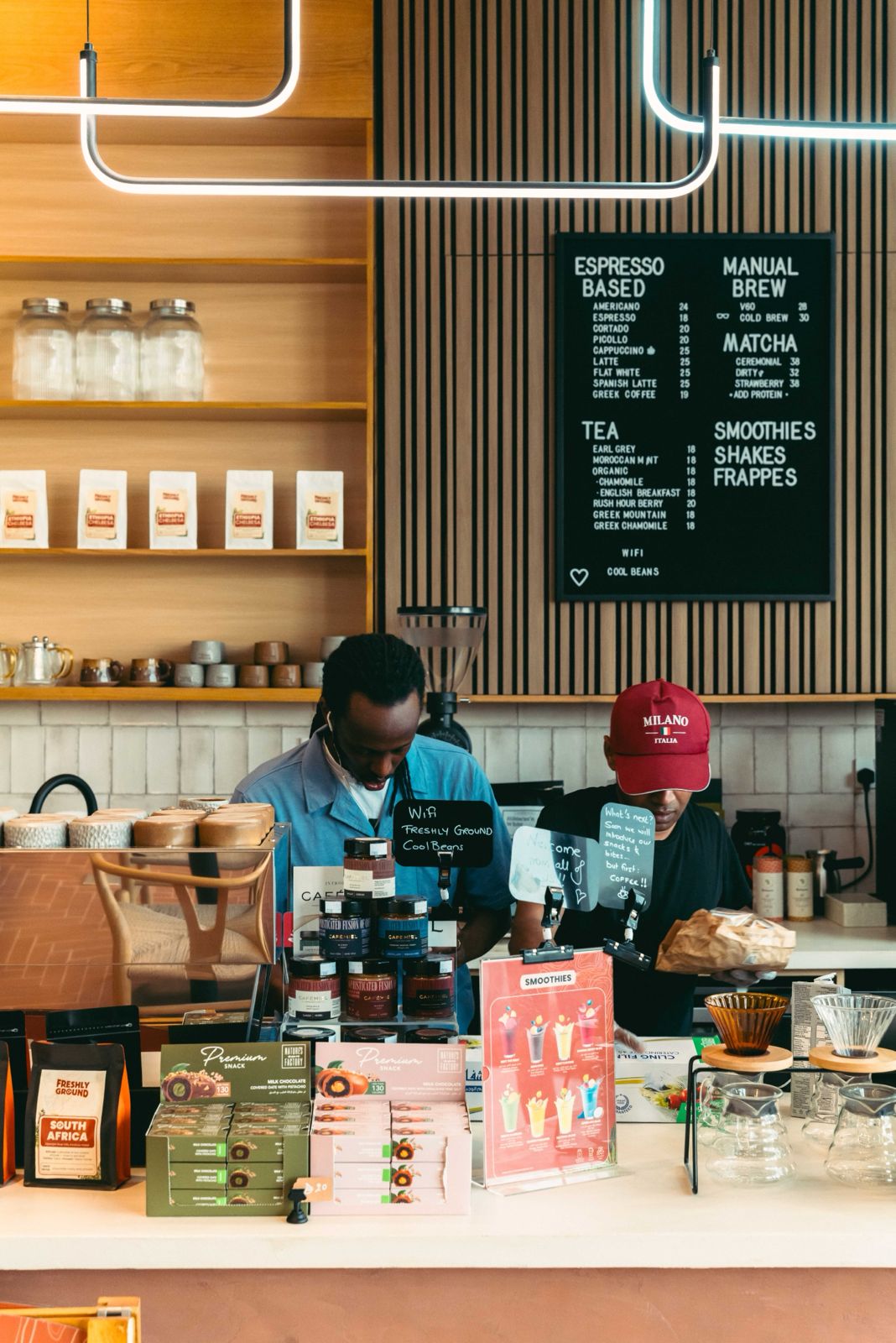 Two Freshly Ground baristas preparing drinks behind the counter, below a chalkboard menu of espresso, brew and matcha drinks