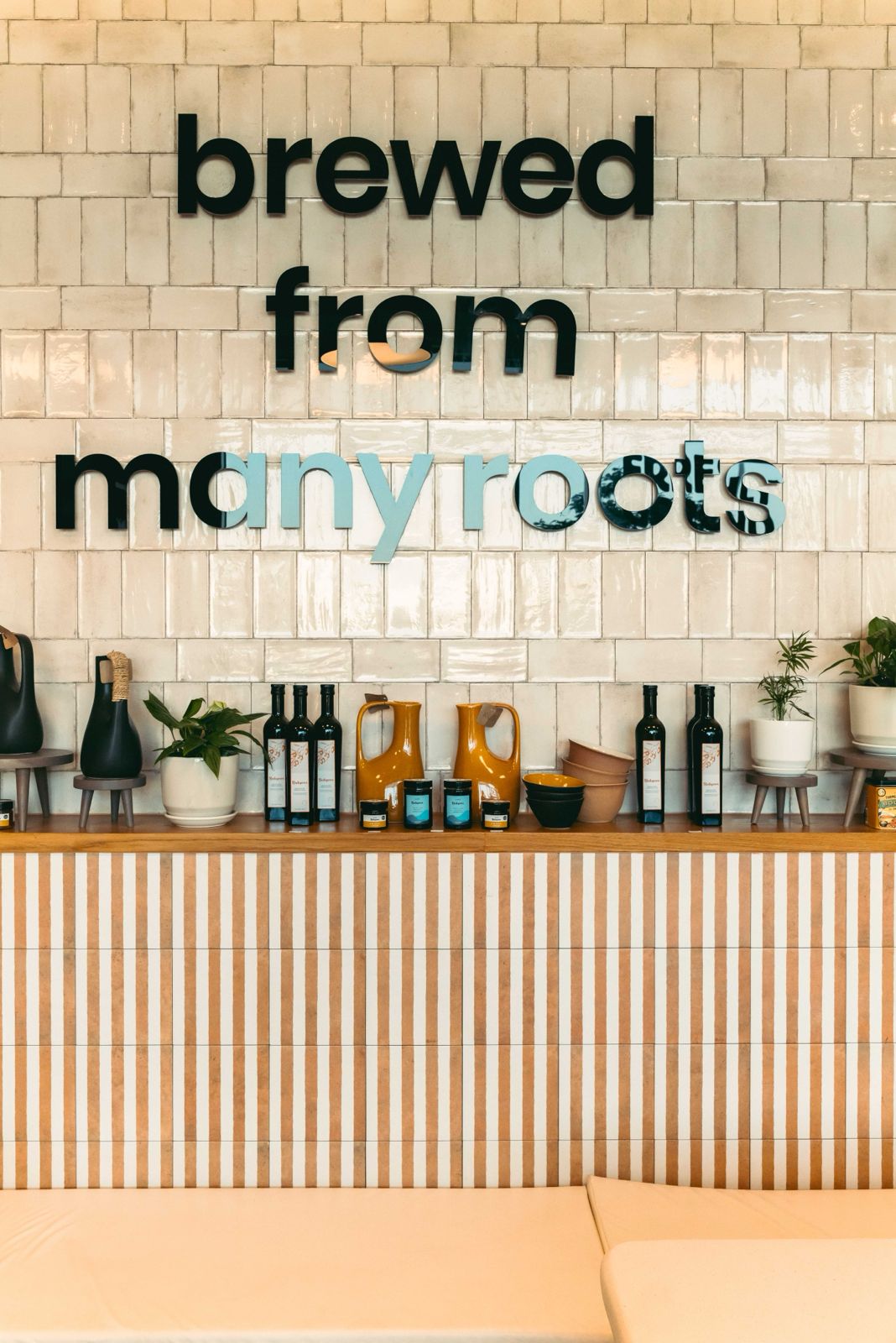 The tiled 'brewed from many roots' feature wall at Freshly Ground, lined with olive oil, ceramic jugs and retail treats