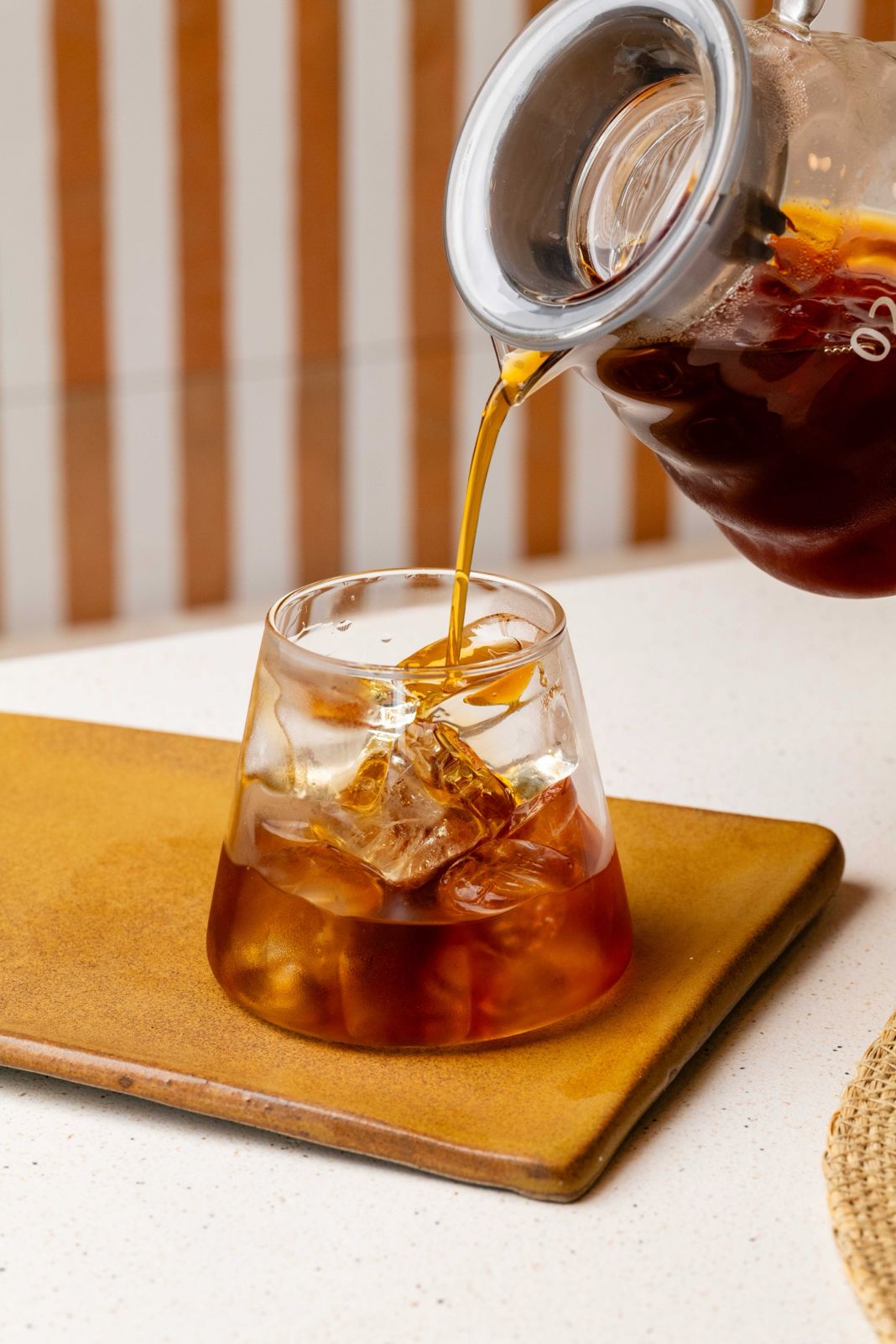 Cold brew coffee being poured from a glass carafe over ice at Freshly Ground