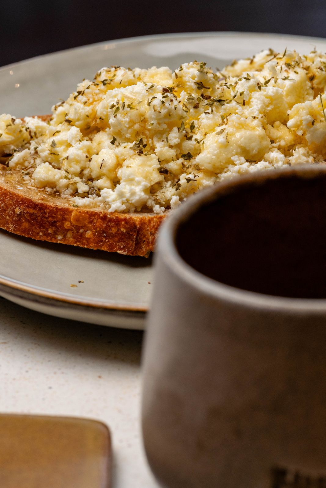Feta toast on sourdough with organic oregano and honey, served beside a Freshly Ground ceramic mug