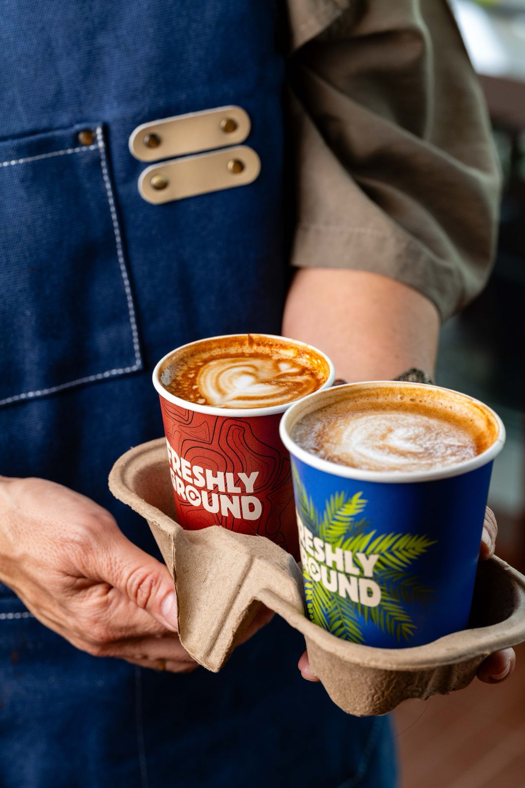 Two Freshly Ground branded takeaway cups with latte art, held in a paper carry tray