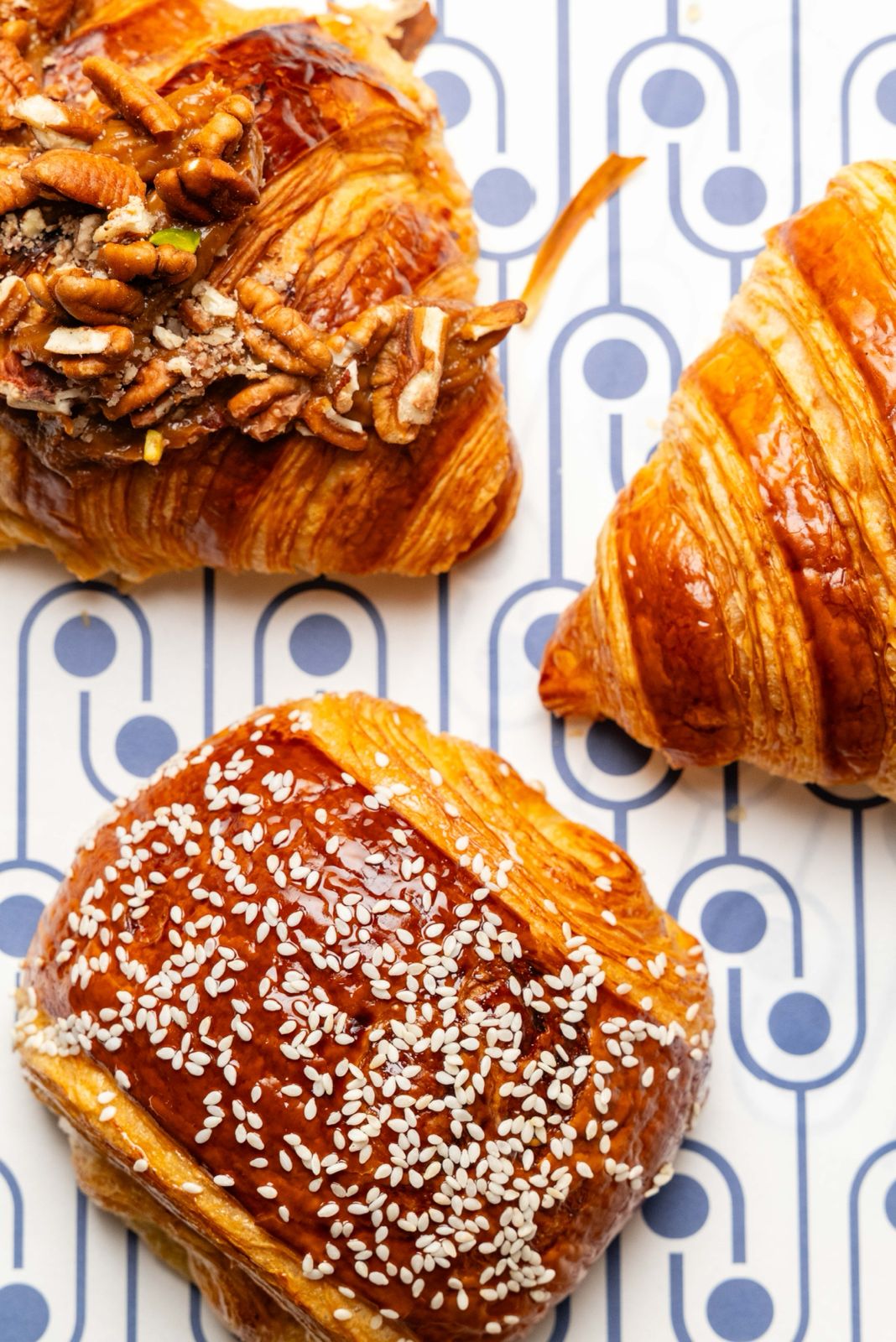 Freshly baked croissants and pastries, including a pecan caramel croissant, arranged on a patterned tile surface